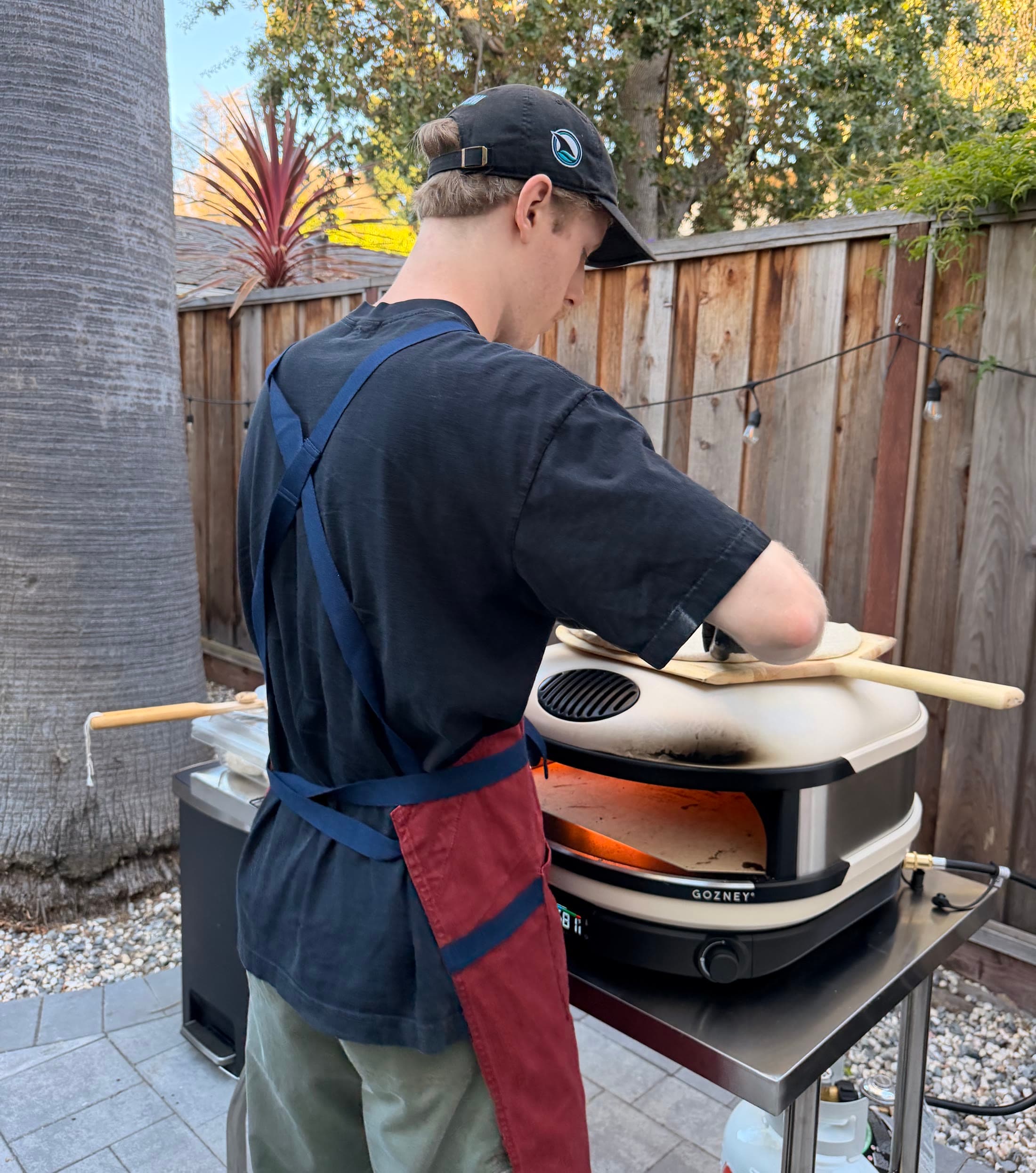 Scuf in his apron sliding a pie into the live-fire oven.