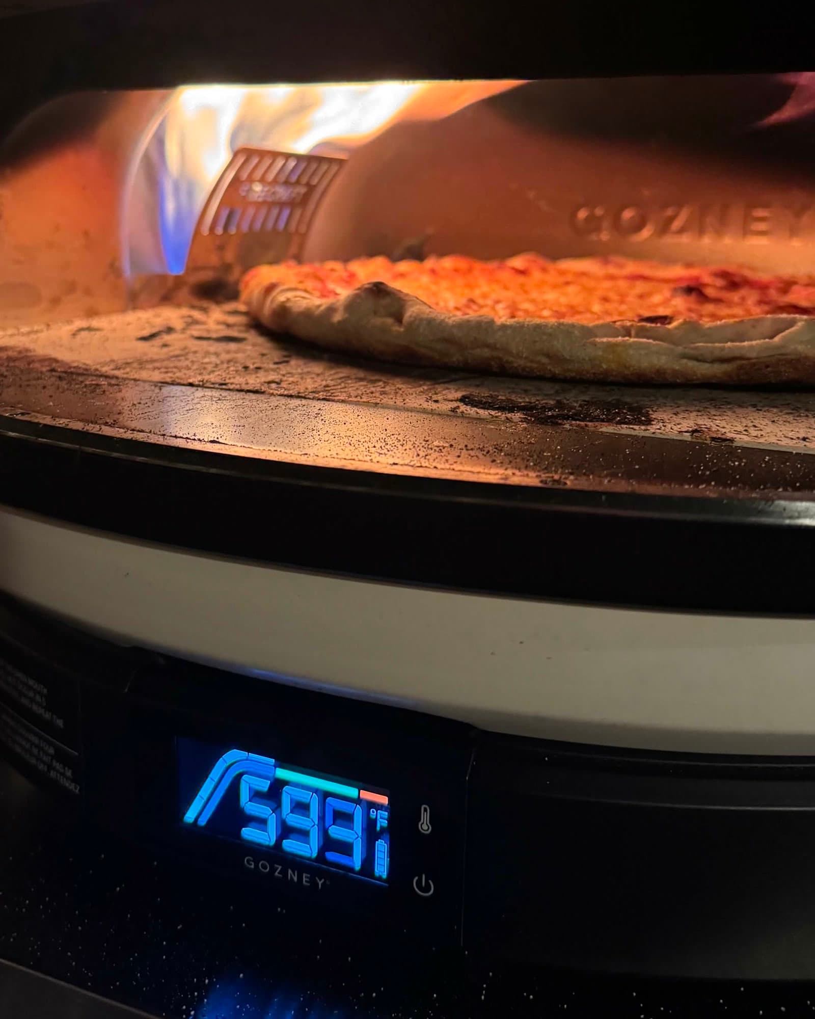 A pie baking inside the Gozney oven, flame behind it, the display reading 599°F.